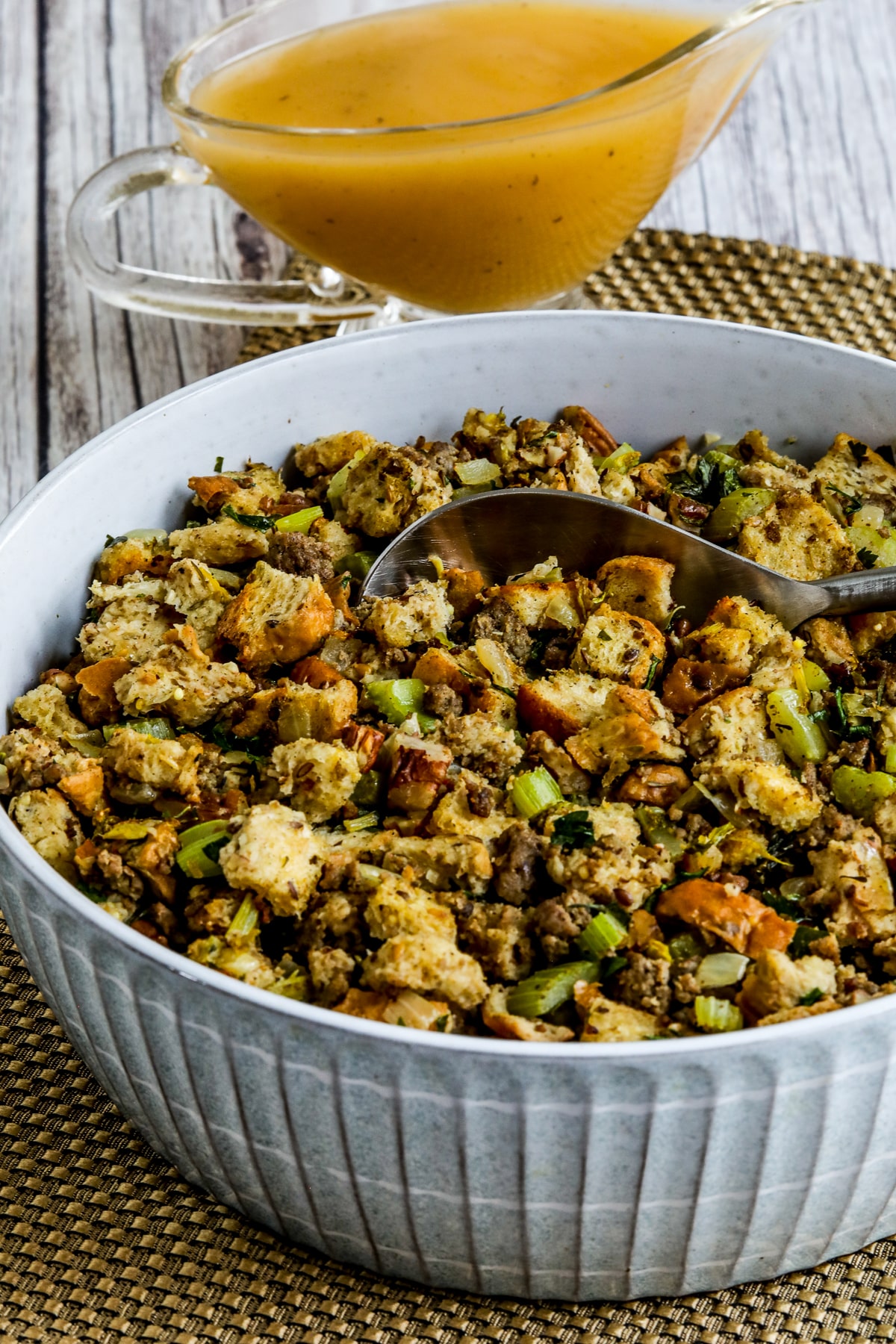 Low-Carb Stuffing (with Sausage and Pecans) shown in serving bowl with spoon and gravy in back.